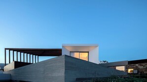 A modern building with a prominent concrete structure, a large window, and a stone facade. - Pnoes Tinos  (Tinos)
