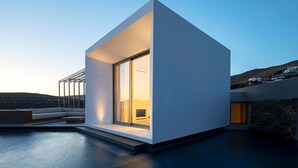 A modern, minimalist building with a large glass window and a flat roof. - Pnoes Tinos  (Tinos)