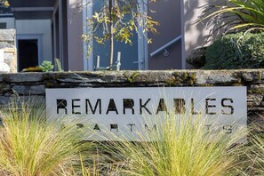 Une pancarte portant l’inscription « REMARKABLES PARTM 19 » est placée devant un mur de pierre, avec de l’herbe et un bâtiment en arrière-plan.
