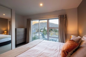Ein Schlafzimmer mit Bett, Schminktisch, einem Balkon mit Stühlen und Blick auf einen Berg.