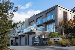 Ein modernes Mehrfamilienhaus mit Steinaußenwand, Balkonen und einer Garage.