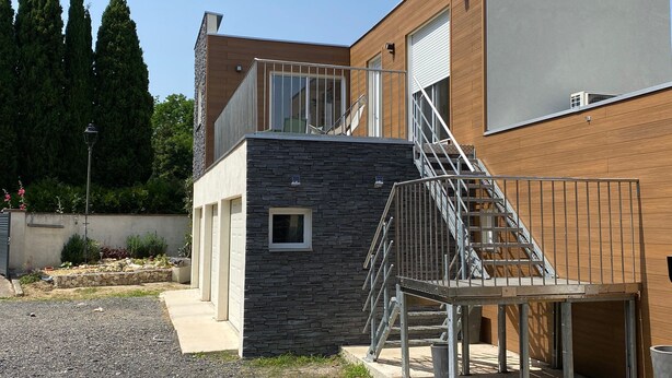 Un edificio moderno con fachada de piedra, una escalera de metal y una puerta de garaje.