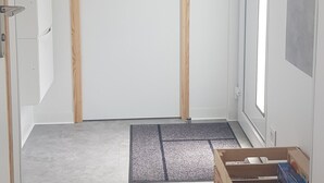 Un pasillo con una puerta de madera, un felpudo pequeño en la entrada y una caja de madera con objetos.