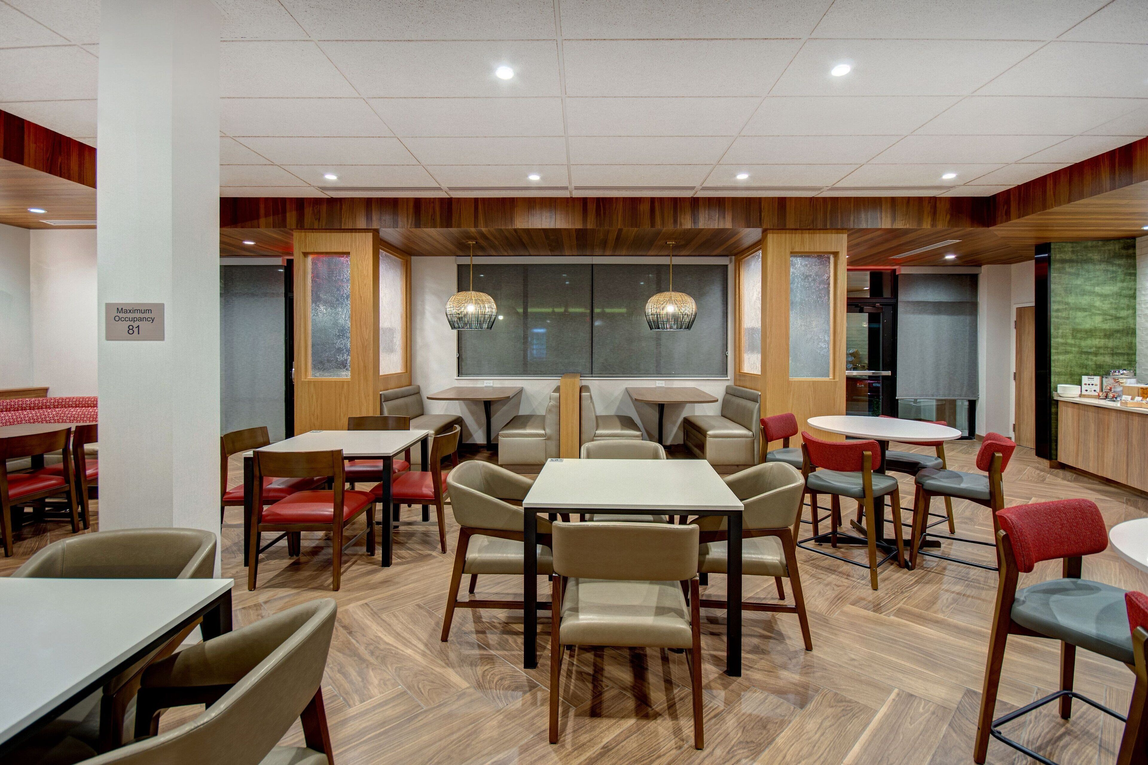 Un restaurante con varias mesas y sillas, suelo de madera y un letrero que indica la ocupación máxima.