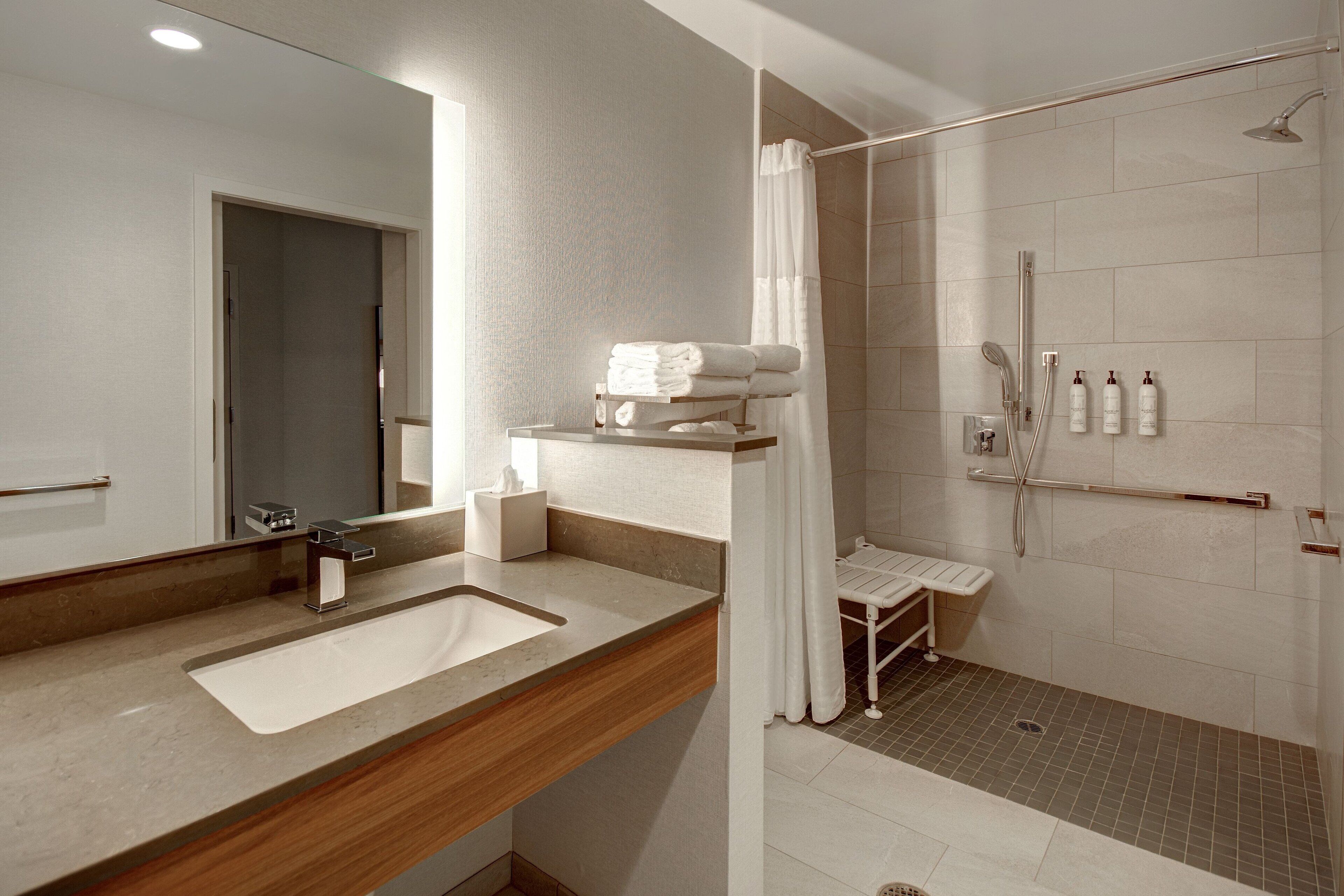 A modern bathroom with a sink, mirror, shower, and towel rack.