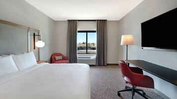 A hotel room with a large bed, a desk, a chair, a TV, and a window with curtains.