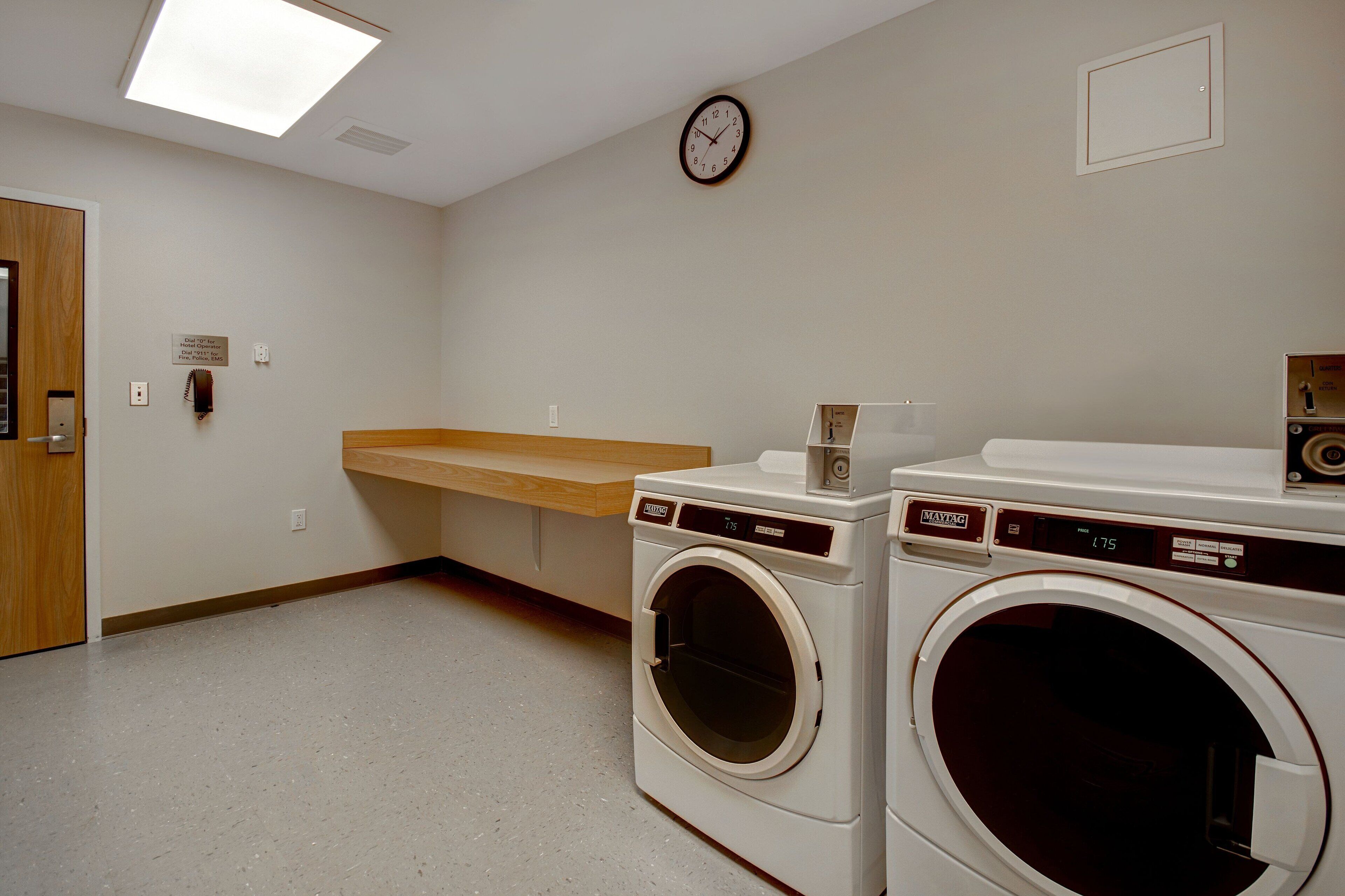 A laundry room with two front-loading washing machines, a wooden bench, a clock, and a door.