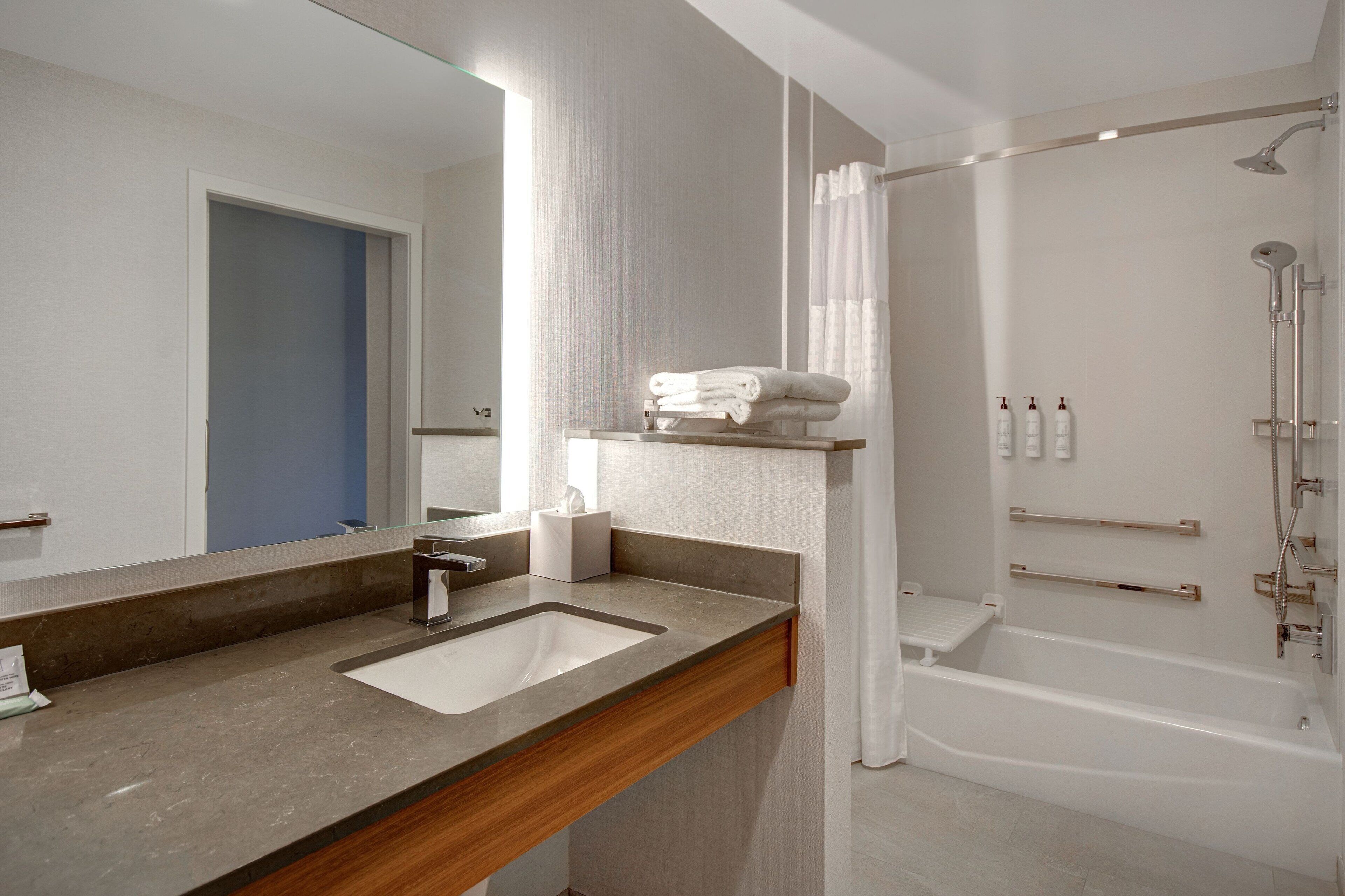 A modern bathroom with a large mirror, a sink, a bathtub, and a shower.
