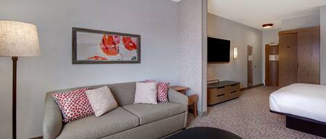 A hotel room with a sofa, a flat-screen TV, a bed, a desk, and a lamp.