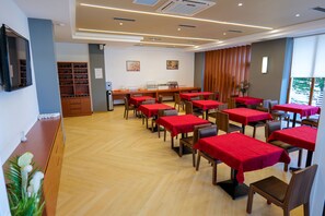 A dining area with multiple tables and chairs, a counter with a display case, and a wall-mounted television. - 6 Milje Hotel (Ksamil)