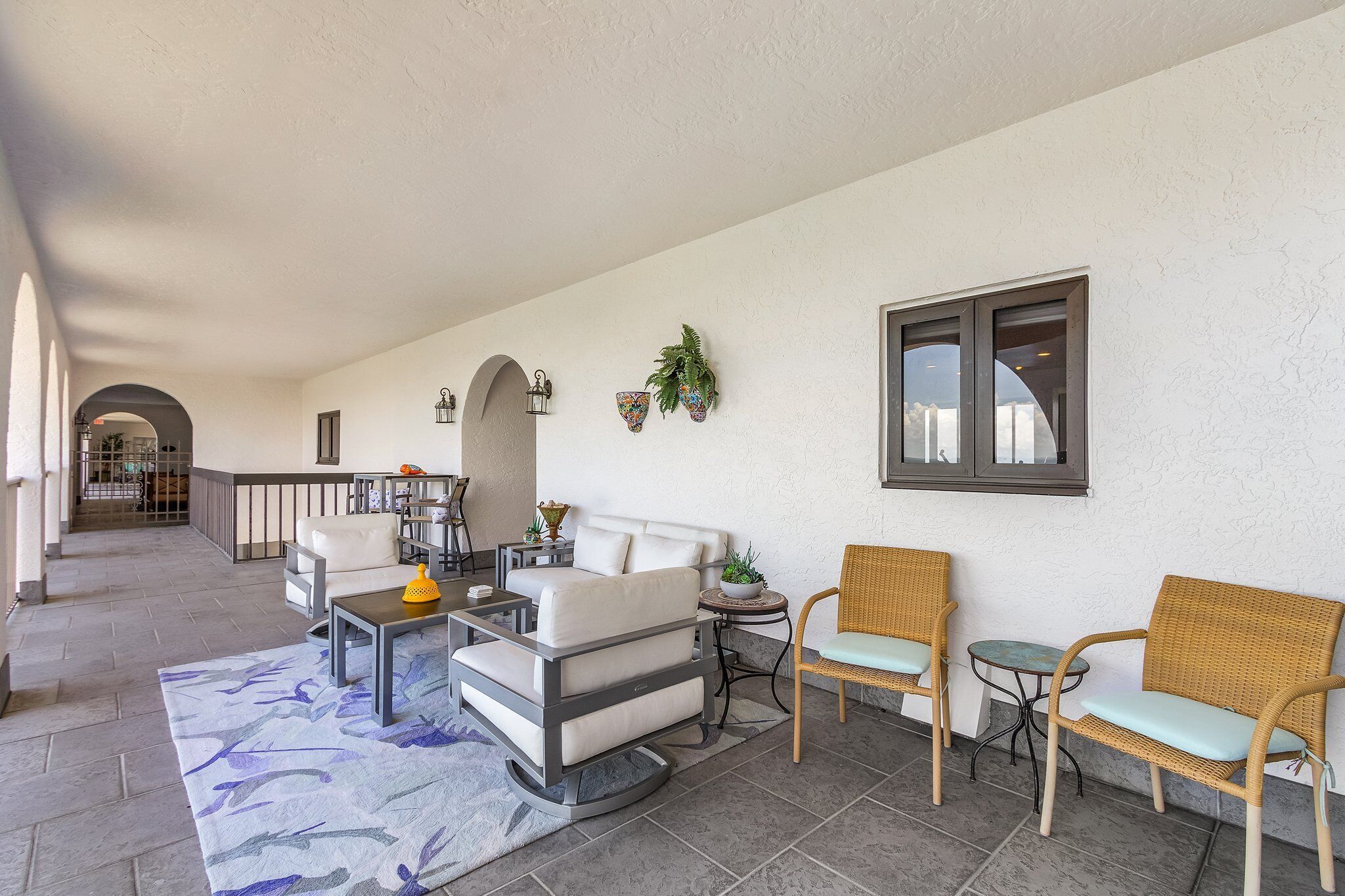 A spacious patio with a sofa, chairs, and a small table, featuring a view of the interior through an archway.