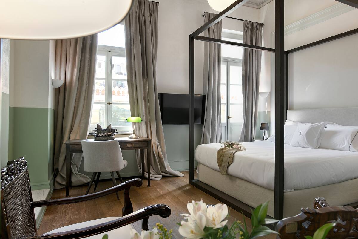 Un lit à baldaquin avec un téléviseur fixé au-dessus, un bureau avec une chaise et une fenêtre avec des rideaux.