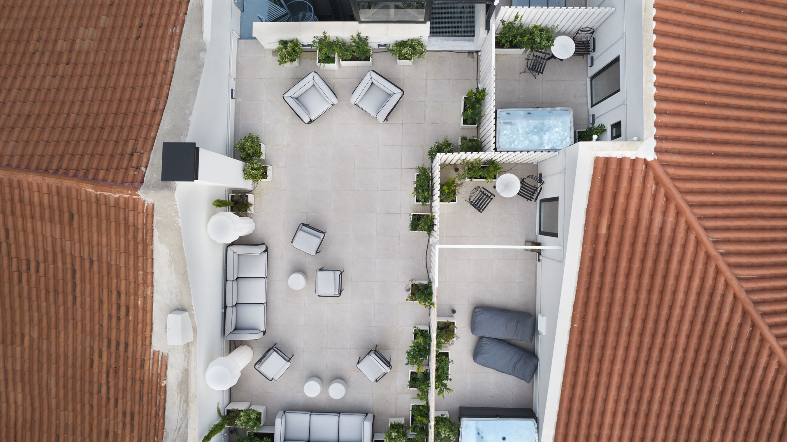 An aerial view of a rooftop patio with multiple seating areas, planters, and a water feature.