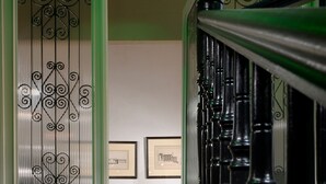 Een trap met versierde zwarte balustrades die leidt naar een kamer met een bank en ingelijste foto's aan de muur.