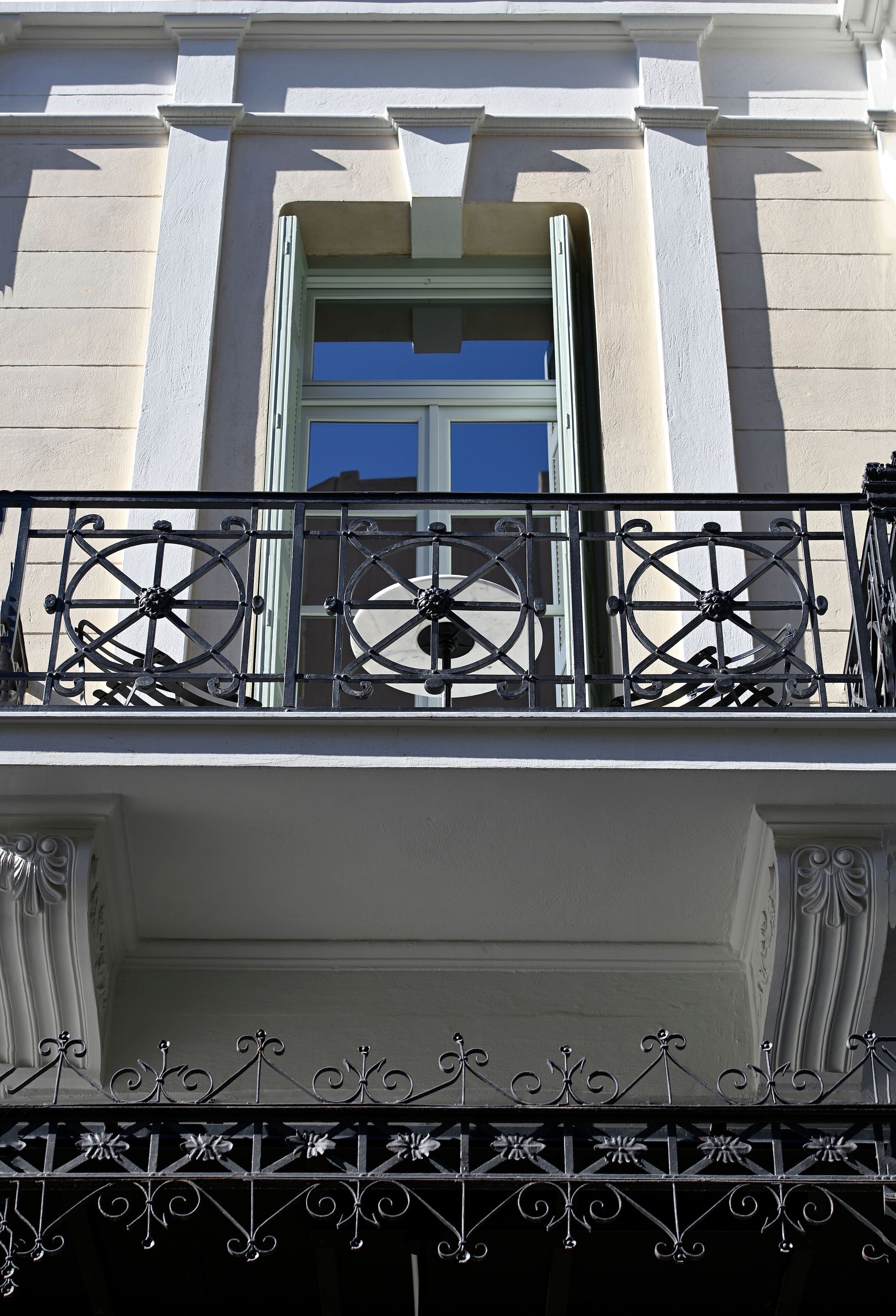 A balcony with ornate wrought iron railings and a window with a blue frame.
