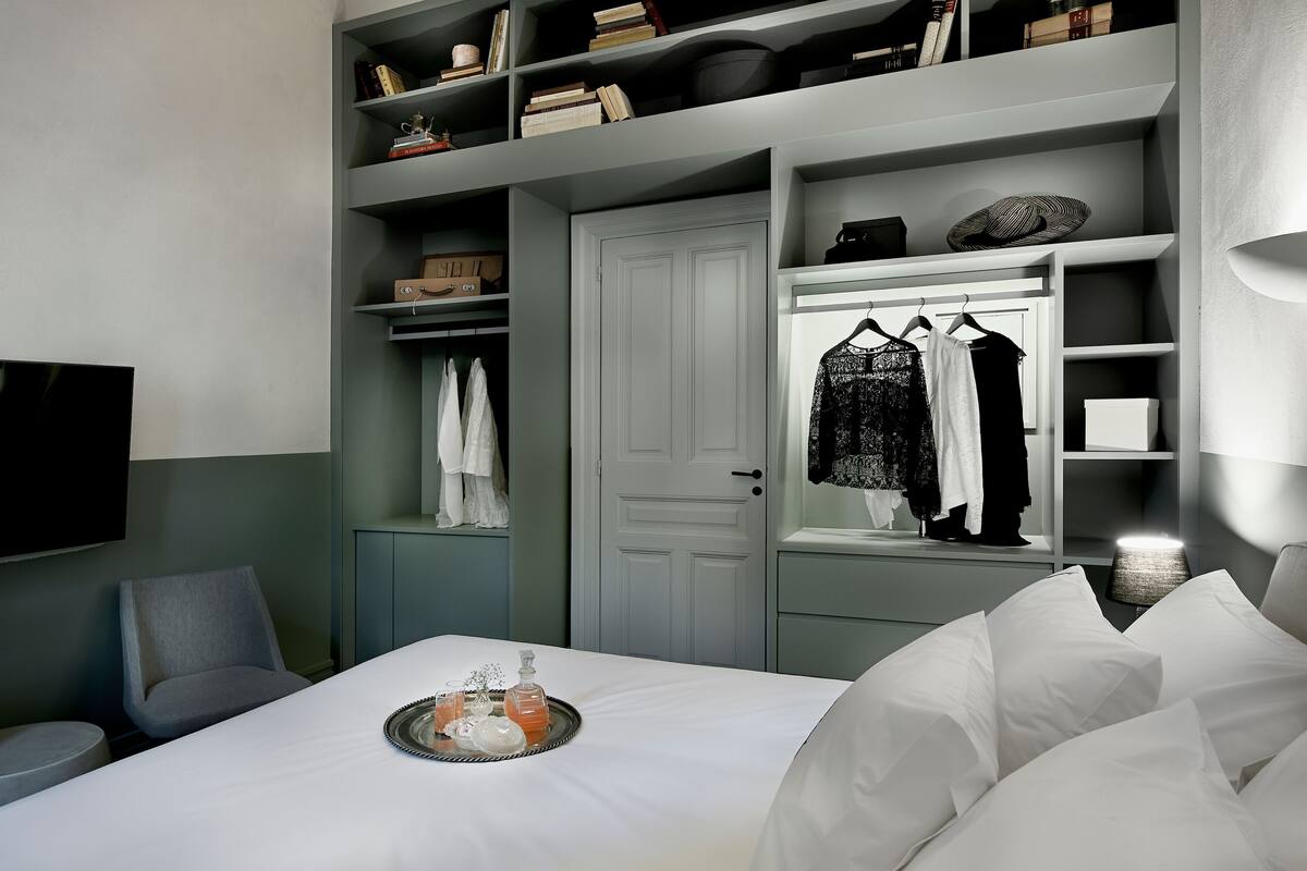 Une chambre d’hôtel équipée d’un lit, d’une télévision, d’une armoire et d’une étagère avec des livres et des objets décoratifs.