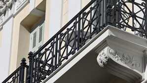 Een gevel met een balkon, voorzien van gedetailleerde zwarte metalen hekwerken en decoratieve witte architectonische details.