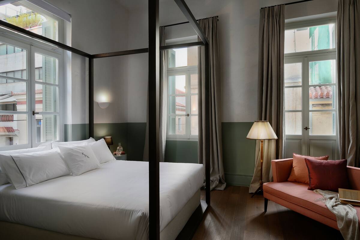 Une chambre d’hôtel avec un grand lit, un canapé et deux fenêtres équipées de rideaux.