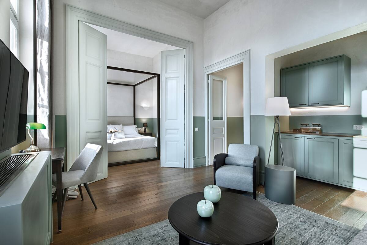 Une chambre d’hôtel moderne comprenant un lit, un coin salon avec une table et des chaises, un coin cuisine et un téléviseur.
