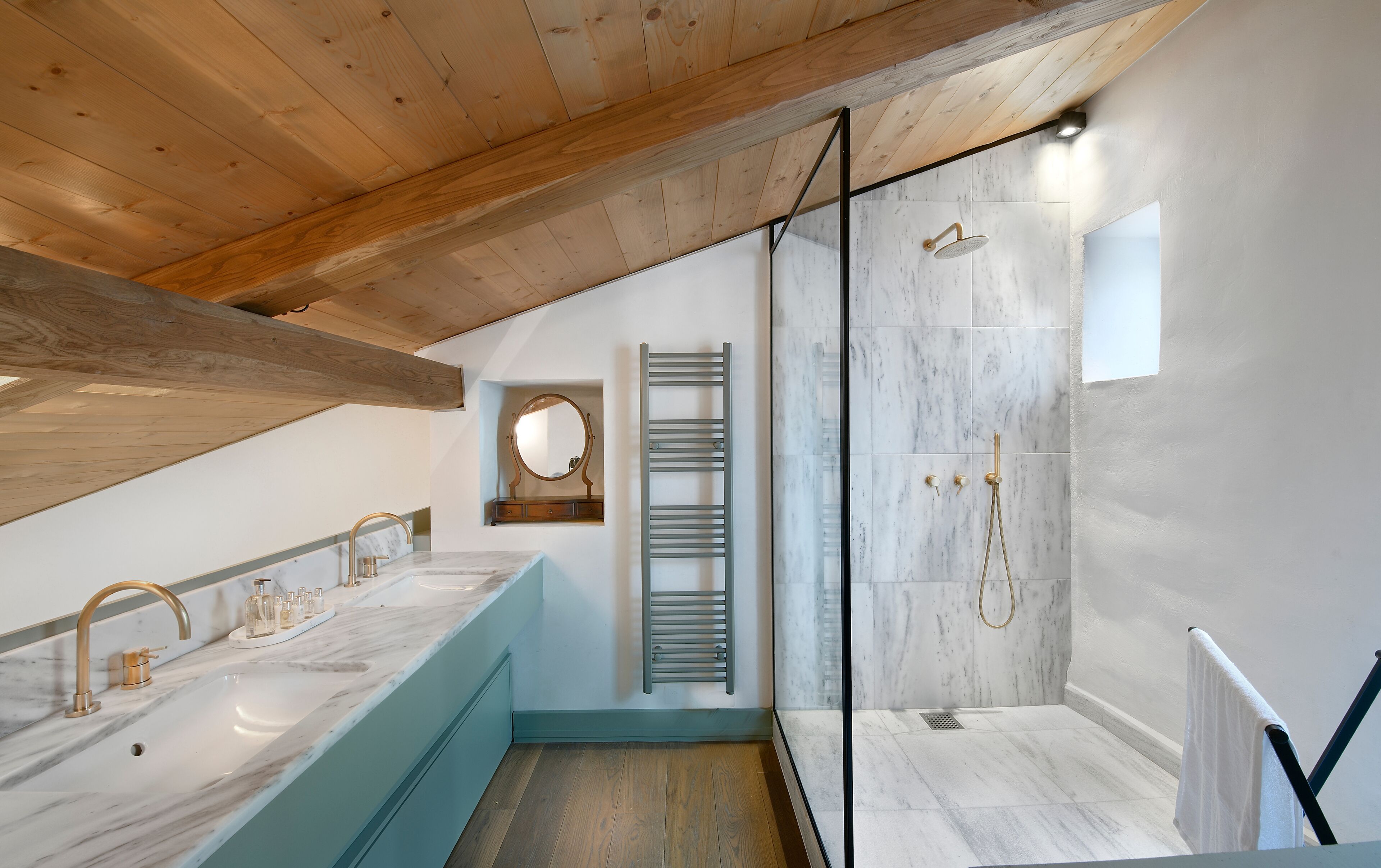 Ein modernes Badezimmer mit Holzboden, Marmorplatten, einer Glasdusche und einem Handtuchhalter.