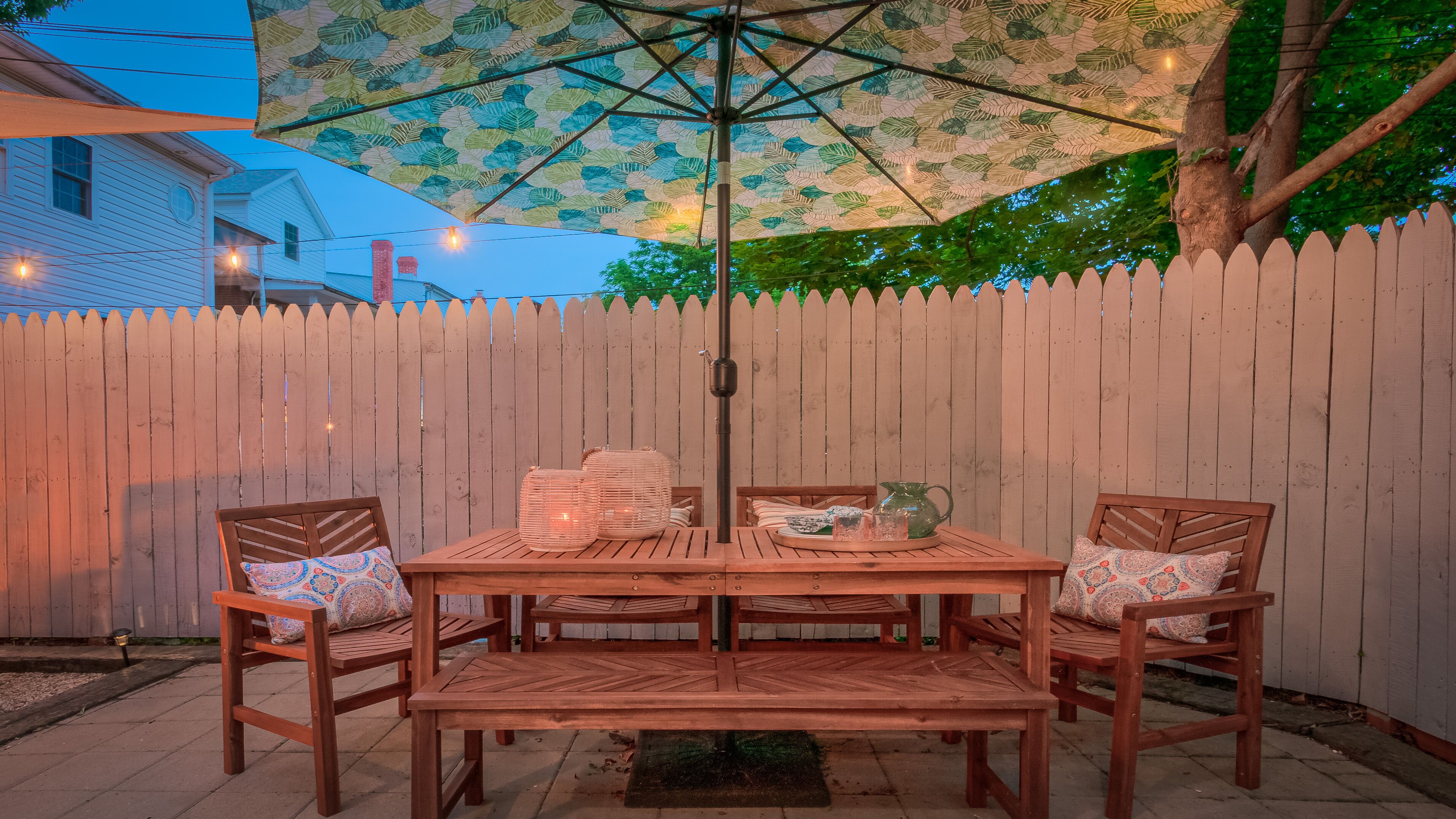 A wooden patio with a table and chairs, a decorative umbrella, and a wooden fence in the background.
