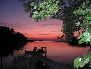 A wooden dock extending into a calm body of water with chairs and a table, surrounded by trees. - 10 Acre 3 BR Waterfront Retreat on Thicket Creek has dock & neighborhood beach
(Onancock)