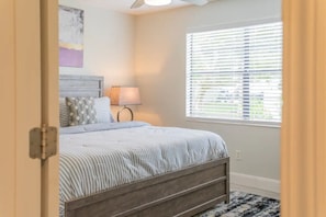 Ein Schlafzimmer mit einem Bett, einem Nachttisch, einer Lampe, einem Fenster mit Jalousien und einem Deckenventilator.