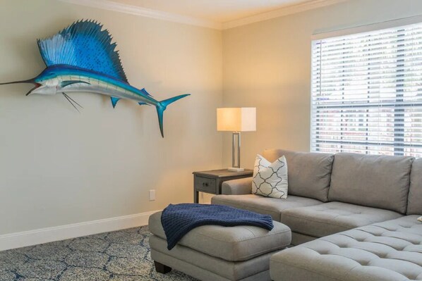 Ein Wohnzimmer mit einer großen Wandfischskulptur, einer Couch, einem Beistelltisch mit Lampe und einem Fenster mit Jalousien.