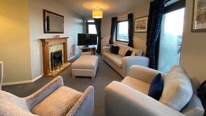 A living room with a fireplace, sofas, a television, and a large window with curtains.