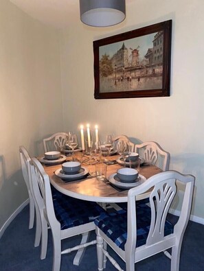 A dining area with a round table set for four, white chairs, and a painting of a cityscape on the wall. - Harbour View, 50m to the Beach and free Parking!  (Nairn)