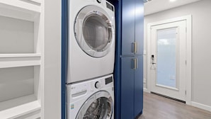 A laundry room with stacked washers and dryers, a blue cabinet, and a door with a window. - Emerald Indigo House | Pet Friendly (Dallas)