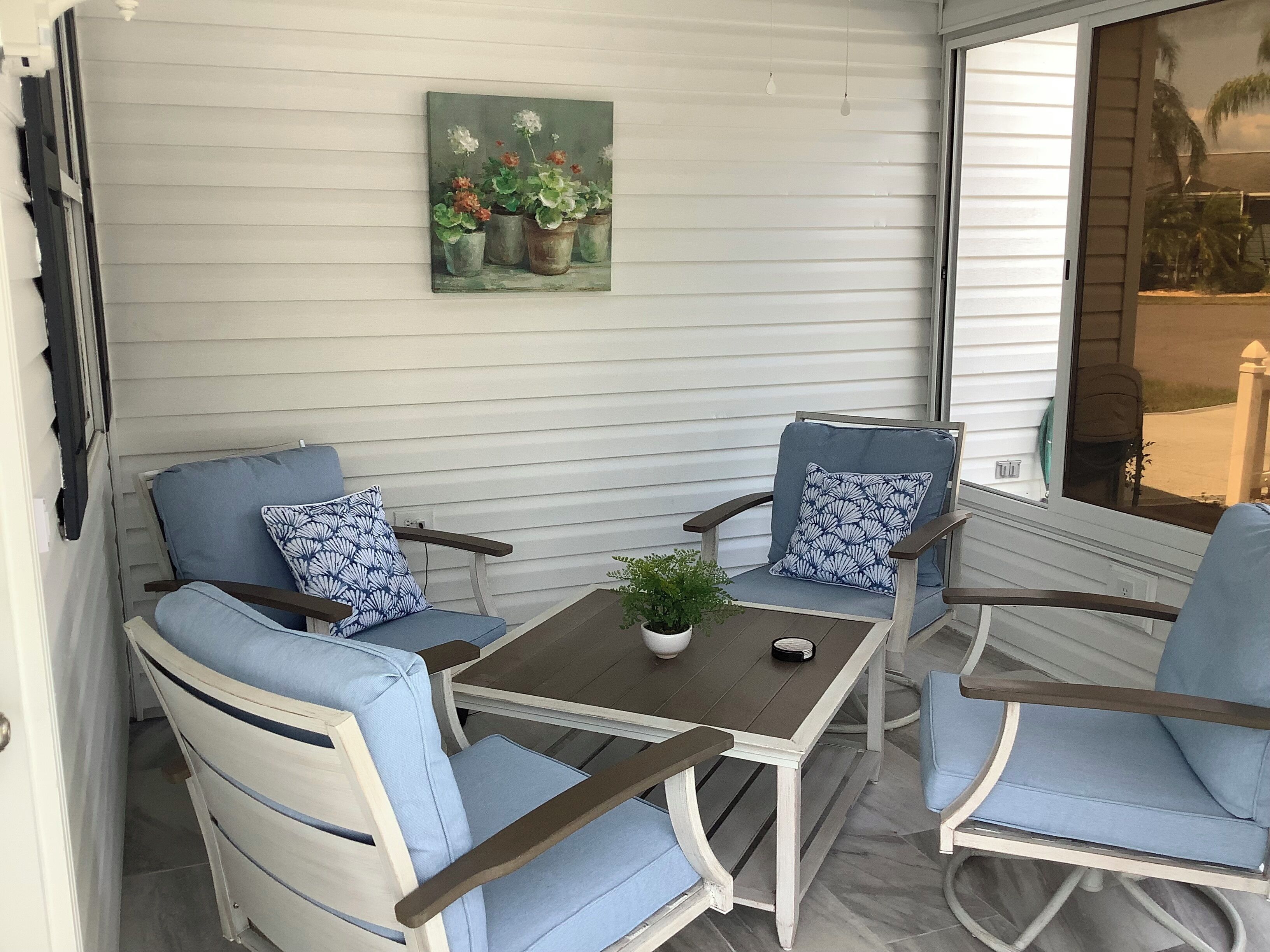 Un patio con dos sillas azules acolchadas, una mesita y una planta en maceta.