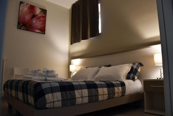 A neatly made bed with a checkered bedspread, two bedside lamps, and a wall-mounted painting of flowers. - Villa 18 - One-Bedroom House (Matera)
