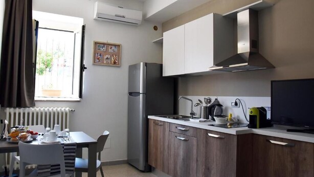 A modern kitchen with a refrigerator, stove, and a dining area with a table and chairs. - Villa 18 - One-Bedroom House (Matera)