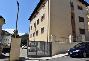 A multi-story building with a beige facade, a gated entrance, and a parked car. - Villa 18 - One-Bedroom House (Matera)