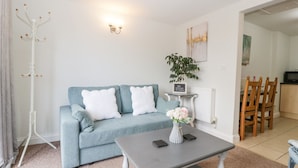 A living room with a light blue sofa, a grey coffee table, a white coat rack, and a small side table with a plant and a sign. - Thornhills Cottage (Bridgwater)