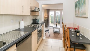 A modern kitchen with a stove, oven, and a dining area with a table and chairs. - Thornhills Cottage (Bridgwater)