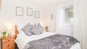 A neatly arranged bedroom with a bed, bedside tables, and a window with curtains. - Thornhills Cottage (Bridgwater)