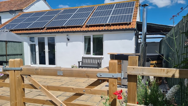 A house with solar panels on the roof, a wooden gate, and a garden with flowers. - Thornhills Cottage (Bridgwater)