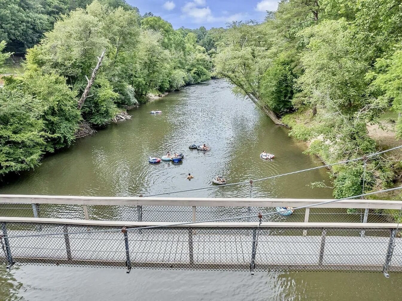 A river with boats and people, surrounded by trees, viewed from a bridge.