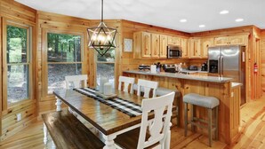 A wooden cabin interior with a dining table, chairs, a kitchen area with a refrigerator, microwave, and bar stools. - Family Cabin Fun: Deck Slide, Hot Tub, Fire Pit & Resort Amenities! (Ellijay)