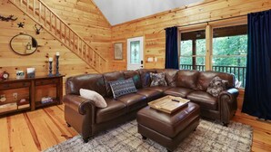 A cozy wooden cabin interior with a brown leather sectional sofa, a wooden coffee table, and a staircase leading to the upper level. - Family Cabin Fun: Deck Slide, Hot Tub, Fire Pit & Resort Amenities! (Ellijay)