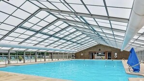 An indoor swimming pool with a glass ceiling, lounge chairs, and a lifeguard chair. - Family Cabin Fun: Deck Slide, Hot Tub, Fire Pit & Resort Amenities! (Ellijay)