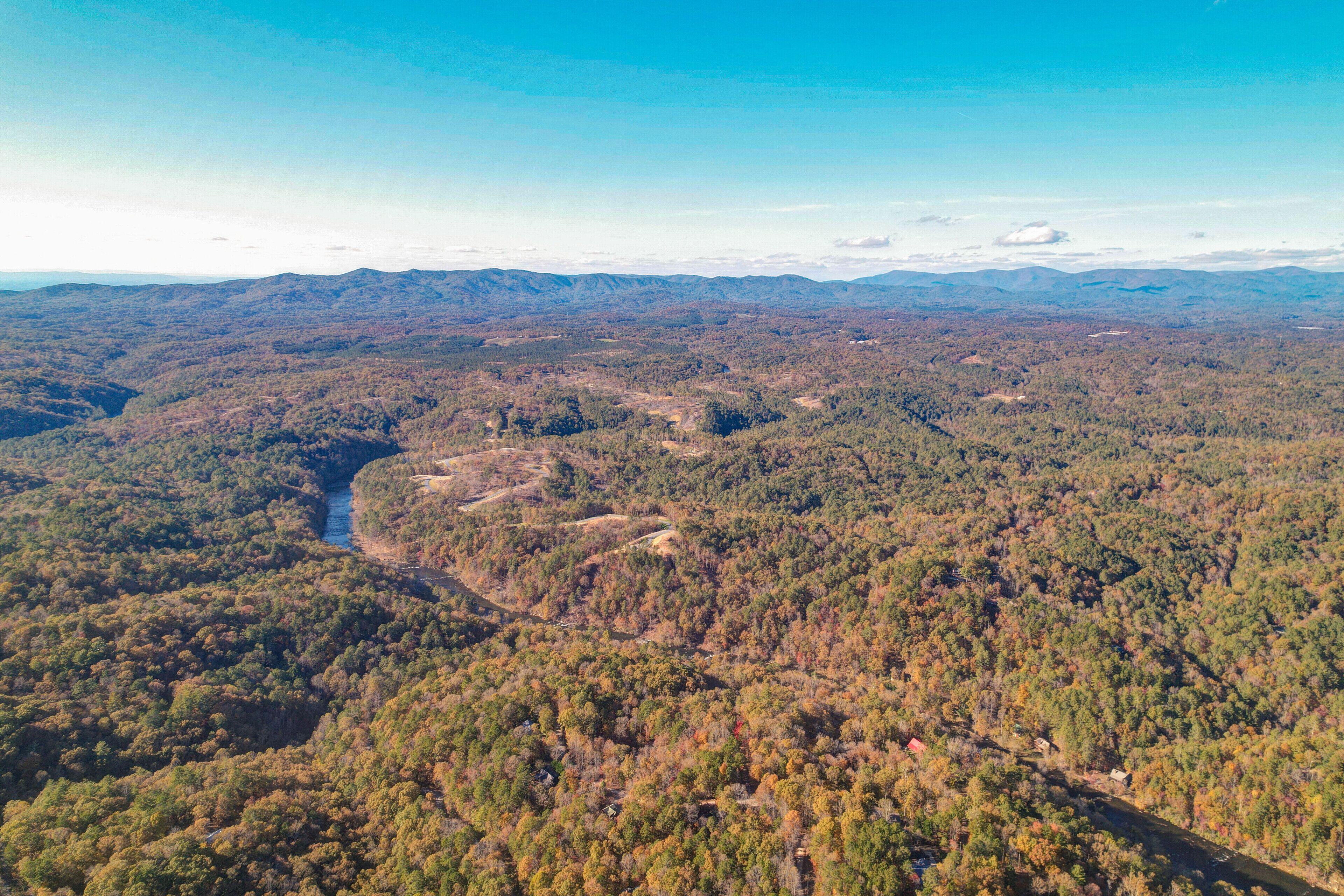 An aerial view of a forested area with a winding road and a small building visible in the distance.