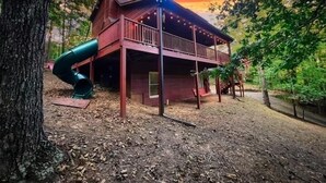 A wooden cabin with a balcony and a slide, surrounded by trees. - Family Cabin Fun: Deck Slide, Hot Tub, Fire Pit & Resort Amenities! (Ellijay)