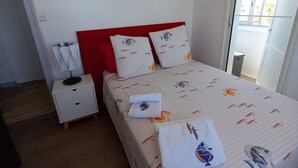A bedroom with a bed, a nightstand, a red headboard, a sun-shaped wall decoration, and a window with a view. - La Goelette 4 (Toulon)