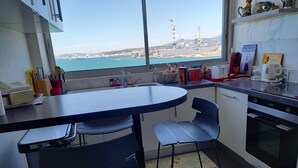 A kitchen with a view of the sea, a dining table, chairs, and a refrigerator. - La Goelette 4 (Toulon)