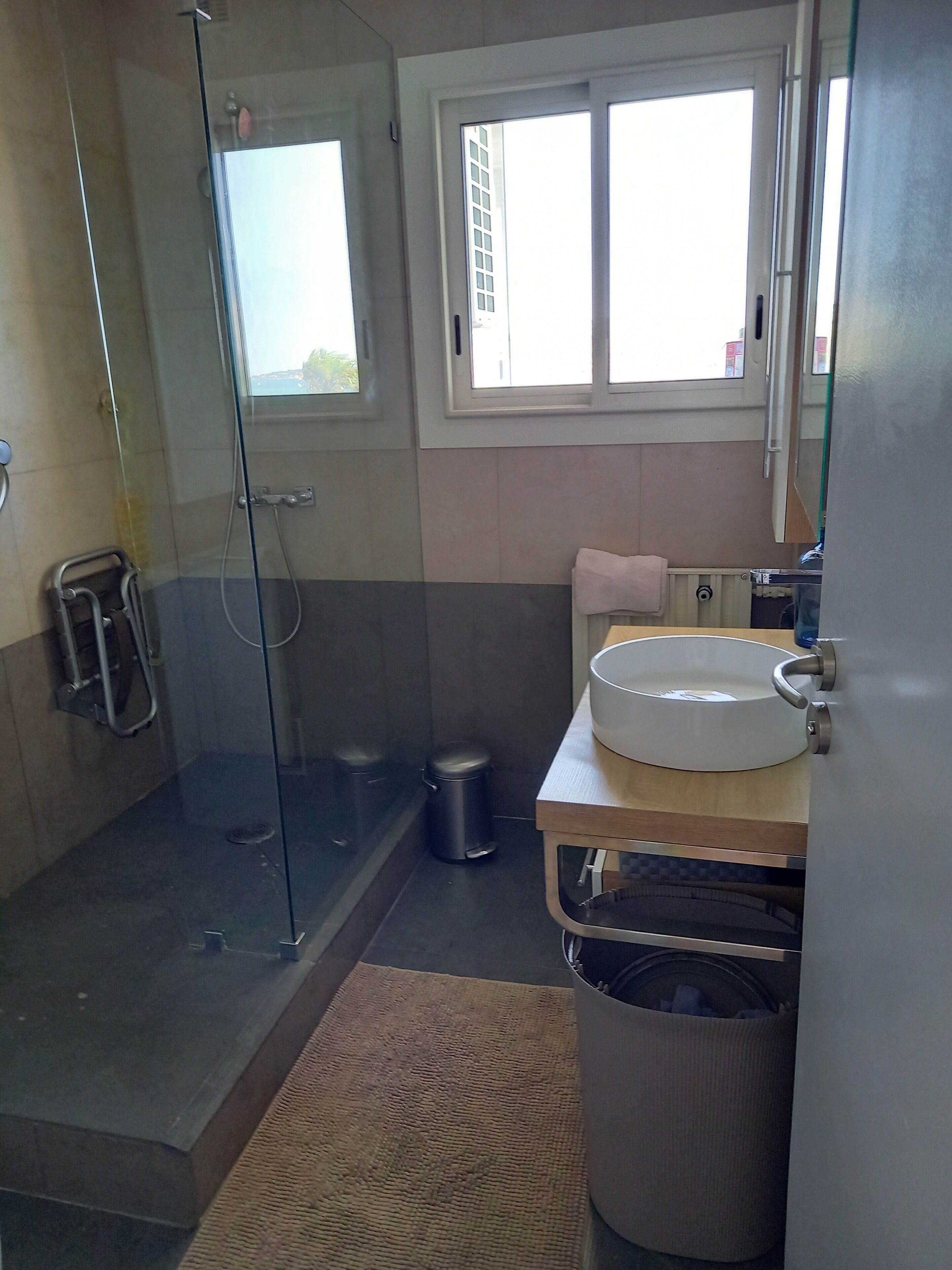 Een badkamer met een douchecabine, een wastafel, een prullenbak en een raam.