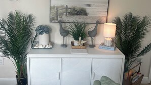 Ein Wohnzimmer mit einem weißen Schrank, einem Strandbild und zwei Zimmerpflanzen.