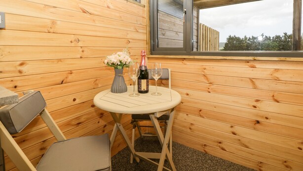 Ein kleines Zimmer aus Holz mit Tisch, Stühlen, einem Fenster und einer Weinflasche.